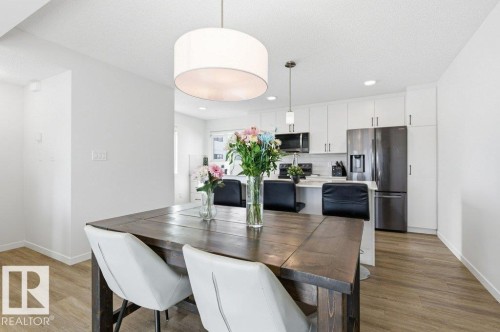 Open-concept living space featuring a modern kitchen with white cabinetry, stainless steel appliances, and a breakfast bar - #49 850 Secord Bv Nw, Edmonton, AB - Indoor Photo Showing Dining Room