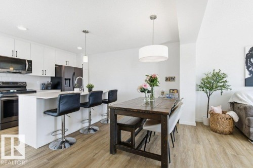 Open-concept living area featuring wood-finish flooring, a kitchen island with seating, pendant lighting, and modern appliances - #49 850 Secord Bv Nw, Edmonton, AB - Indoor