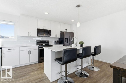 Contemporary kitchen featuring white cabinetry, a kitchen island with seating, a stainless steel sink with gooseneck faucet, black appliances, and wood-finish flooring - #49 850 Secord Bv Nw, Edmonton, AB - Indoor Photo Showing Kitchen With Upgraded Kitchen