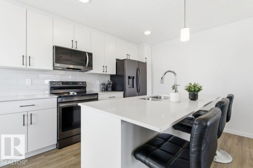 Kitchen featuring white cabinetry, subway tile backsplash, stainless steel appliances, and an island with a built-in sink and pendant lighting - #49 850 Secord Bv Nw, Edmonton, AB - Indoor Photo Showing Kitchen With Double Sink