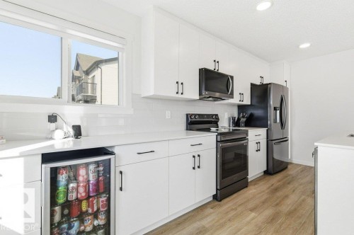 Contemporary kitchen featuring white cabinetry, a white subway tile backsplash, and light-toned wood-finish flooring - #49 850 Secord Bv Nw, Edmonton, AB - Indoor Photo Showing Kitchen