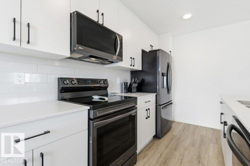 Modern kitchen featuring white cabinetry, dark hardware, white countertops, subway tile backsplash, and wood-finish flooring - #49 850 Secord Bv Nw, Edmonton, AB - Indoor Photo Showing Kitchen
