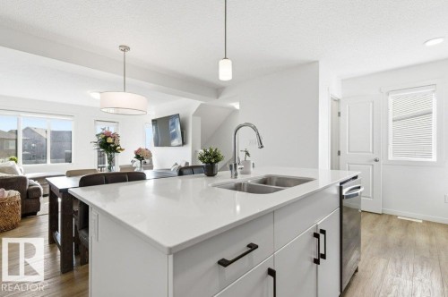 Kitchen island with a white countertop and a double stainless steel sink - #49 850 Secord Bv Nw, Edmonton, AB - Indoor Photo Showing Kitchen With Double Sink