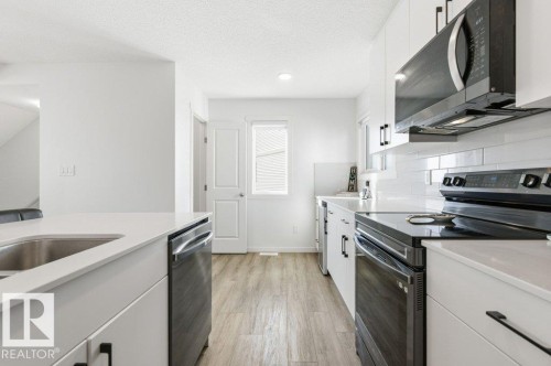 Contemporary kitchen featuring white cabinetry, a stainless steel sink, wood-finish flooring, and black appliances including a range and microwave - #49 850 Secord Bv Nw, Edmonton, AB - Indoor Photo Showing Kitchen