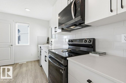 Contemporary kitchen featuring white cabinetry with matte black hardware, a subway tile backsplash, and light-toned countertops - #49 850 Secord Bv Nw, Edmonton, AB - Indoor Photo Showing Kitchen
