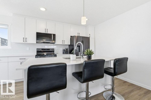 Modern kitchen featuring white cabinetry, a large center island with seating, a white subway tile backsplash, stainless steel appliances, and wood-finish flooring - #49 850 Secord Bv Nw, Edmonton, AB - Indoor Photo Showing Kitchen With Upgraded Kitchen