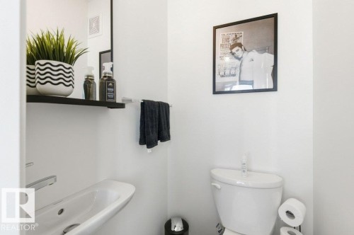 White powder room featuring a wall-mounted sink with chrome faucet, a floating black shelf, and a mirror - #49 850 Secord Bv Nw, Edmonton, AB - Indoor Photo Showing Bathroom