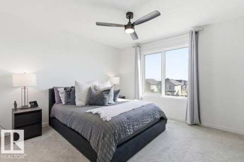 Bedroom featuring a large window, light gray carpeting, a dark-toned ceiling fan, and white walls - #49 850 Secord Bv Nw, Edmonton, AB - Indoor Photo Showing Bedroom