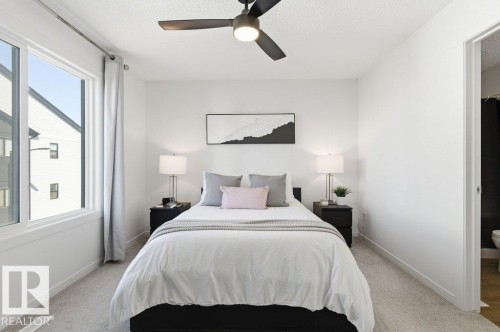 Carpeted room featuring a large window, a modern ceiling fan with lighting, and a white interior door - #49 850 Secord Bv Nw, Edmonton, AB - Indoor Photo Showing Bedroom