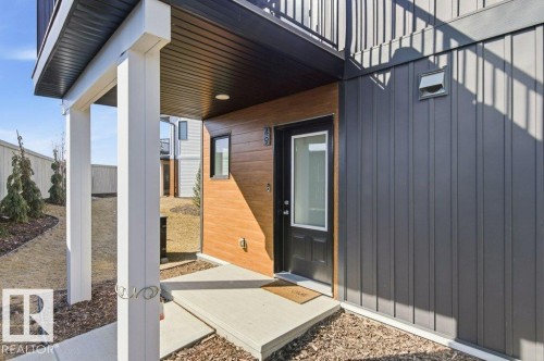 Contemporary exterior featuring vertical panel siding, wood-look accent paneling, and a covered entry with white support columns - #49 850 Secord Bv Nw, Edmonton, AB - Outdoor With Exterior