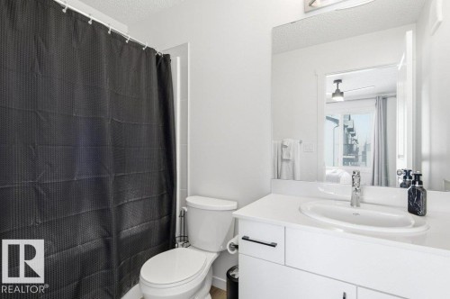 Bathroom featuring a white vanity with a single basin sink, a large mirror, a toilet, and a tiled shower with a dark shower curtain - #49 850 Secord Bv Nw, Edmonton, AB - Indoor Photo Showing Bathroom