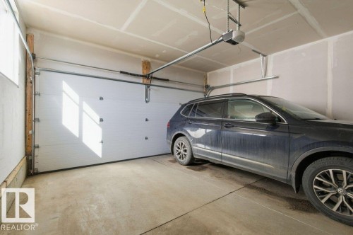 Single-car garage featuring a concrete floor, white panel garage door, automatic garage door opener, and unfinished walls and ceiling - #49 850 Secord Bv Nw, Edmonton, AB - Indoor Photo Showing Garage