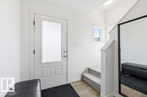 Entryway featuring a solid core door with upper frosted glass, wood-finish flooring, a carpeted staircase, and white trim - #49 850 Secord Bv Nw, Edmonton, AB - Indoor Photo Showing Other Room