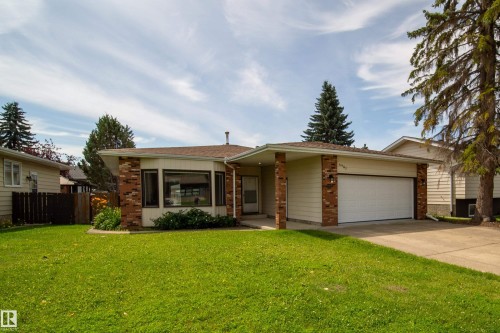 Charming single-story home featuring a brick and vinyl exterior with a wide bay window, two-car garage, and manicured front lawn bordered by mature evergreen trees and established landscaping - 6907 19 Avenue Nw, Edmonton, AB - Outdoor With Facade