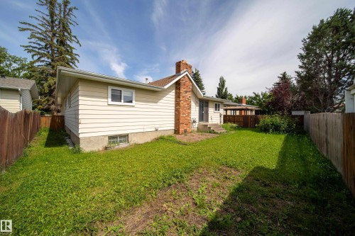Spacious backyard featuring a wood fence, mature perimeter trees, and a brick chimney - 6907 19 Avenue Nw, Edmonton, AB - Outdoor