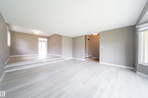Spacious open floor plan showcasing light wood-finish flooring throughout, neutral wall finishes, and abundant natural light from multiple windows - 6907 19 Avenue Nw, Edmonton, AB - Indoor Photo Showing Other Room