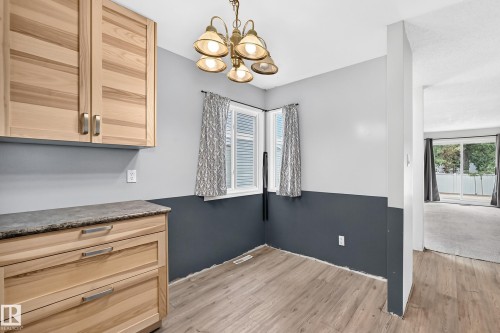 Bright kitchen and dining area featuring natural wood cabinetry with horizontal louvered doors, wood-finish flooring throughout, and a two-tone wall treatment with charcoal wainscoting - 290 Lancaster Terrace Nw, Edmonton, AB - Indoor Photo Showing Other Room