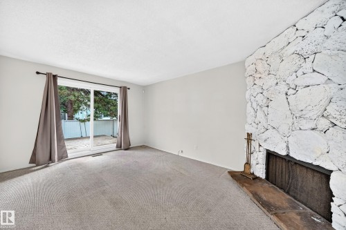 Spacious living room with neutral carpeting, large sliding glass doors opening to outdoor space, and a distinctive white textured stone fireplace feature wall with dark hearth detail - 290 Lancaster Terrace Nw, Edmonton, AB - Indoor With Fireplace