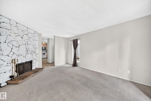 Living area featuring a stone accent wall, fireplace with hearth, and neutral carpeting - 290 Lancaster Terrace Nw, Edmonton, AB - Indoor With Fireplace