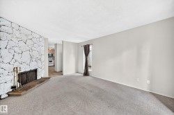 Living area featuring a stone accent wall, fireplace with hearth, and neutral carpeting - 