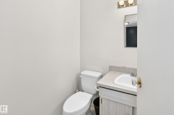 Bathroom featuring a white toilet, light-toned wood-finish vanity, integrated sink, and a wall-mounted mirror with brass-finish lighting - 