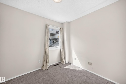 Bright corner bedroom with neutral wall finishes, neutral-tone carpeting, and natural light from a large window with curtain hardware - 290 Lancaster Terrace Nw, Edmonton, AB - Indoor Photo Showing Other Room