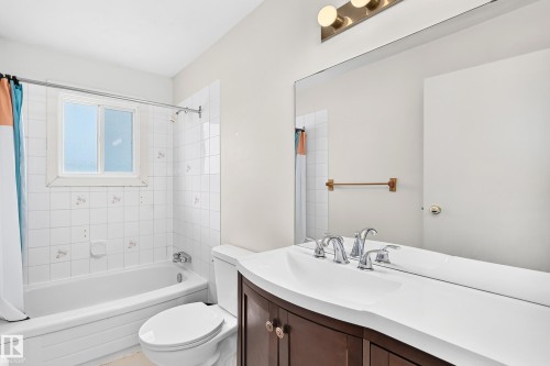 Bathroom featuring a white bathtub with tiled surround, a white toilet, and a vanity with a dark wood-finish cabinet and integrated white sink - 290 Lancaster Terrace Nw, Edmonton, AB - Indoor Photo Showing Bathroom