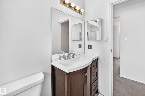 Elegant bathroom vanity featuring a dark wood-finish cabinet with multiple drawers, white porcelain sink, polished chrome faucet fixtures, and ample mirror with brass-finish lighting - 290 Lancaster Terrace Nw, Edmonton, AB - Indoor Photo Showing Bathroom