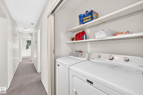 Dedicated laundry room featuring side-by-side washer and dryer with white enamel finish, open shelving with chrome hardware for storage, and gray carpeted flooring - 290 Lancaster Terrace Nw, Edmonton, AB - Indoor Photo Showing Laundry Room