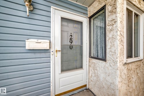 Welcoming entry featuring a white-framed storm door with brass hardware and address numerals, set within horizontal siding in soft blue-gray tones - 290 Lancaster Terrace Nw, Edmonton, AB - Outdoor With Exterior
