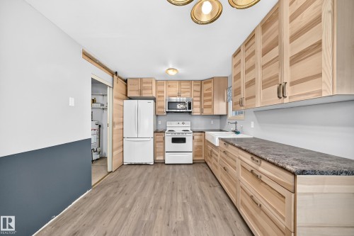 Kitchen featuring ample light wood cabinetry, stone-finish countertops, wood-finish flooring, and a white farmhouse sink - 290 Lancaster Terrace Nw, Edmonton, AB - Indoor Photo Showing Kitchen