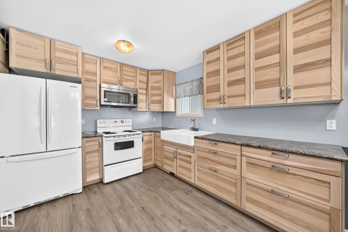 Kitchen featuring natural wood cabinetry, dark speckled countertops, and wood-finish flooring - 290 Lancaster Terrace Nw, Edmonton, AB - Indoor Photo Showing Kitchen