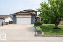 Split-level home featuring a two-car garage, gray brick facade, a tiered front yard with decorative landscaping, a substantial tree, and a concrete driveway - 10711 108 Avenue, Westlock, AB  - Outdoor 