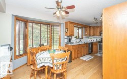 Kitchen dining area featuring a bay window with wood blinds, wood-finish flooring, a ceiling fan, and wood cabinetry - 