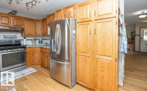 Kitchen featuring wood-finish cabinetry, stainless steel appliances, a tile backsplash, and light wood-finish flooring - 10711 108 Avenue, Westlock, AB - Indoor Photo Showing Kitchen