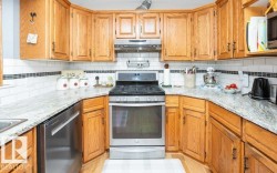U-shaped kitchen featuring light wood cabinetry, white subway tile backsplash with a dark accent stripe, granite-patterned countertops, and a stainless steel range with overhead ventilation - 