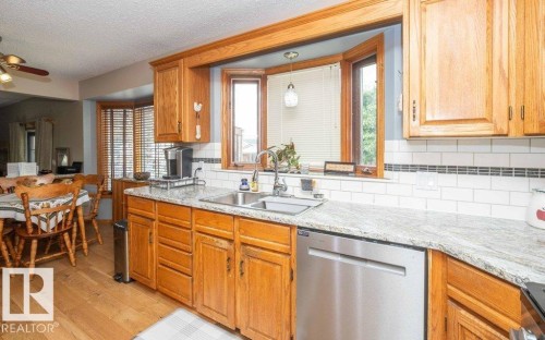 Kitchen featuring a stainless steel double sink, granite-style countertops, wood-finish cabinetry, a subway tile backsplash, and wood-finish flooring - 10711 108 Avenue, Westlock, AB - Indoor Photo Showing Kitchen With Double Sink