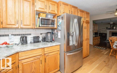 Kitchen featuring wood cabinetry, light-toned countertops, subway tile backsplash with accent band, and wood-finish flooring - 10711 108 Avenue, Westlock, AB - Indoor Photo Showing Kitchen