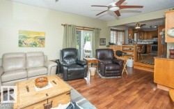 Living area featuring wood-finish flooring, a ceiling fan with integrated lighting, and a glass-paneled exterior door - 