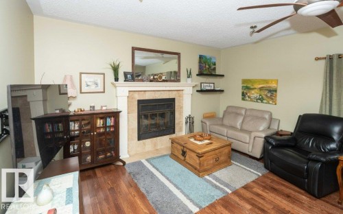 Living area featuring a fireplace with a stone surround and mantel, wood-finish flooring, a ceiling fan, and built-in wall shelves - 10711 108 Avenue, Westlock, AB - Indoor Photo Showing Living Room With Fireplace