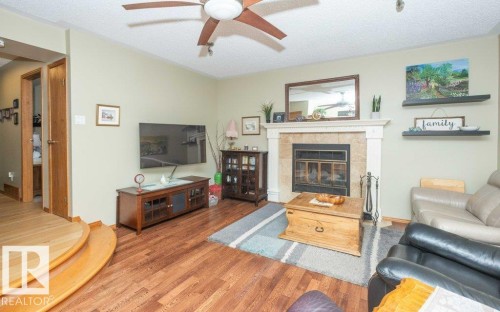 Living area featuring wood-finish flooring, a ceiling fan with light fixture, and a fireplace with a stone surround and white mantel - 10711 108 Avenue, Westlock, AB - Indoor Photo Showing Living Room With Fireplace