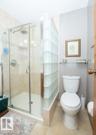 Bathroom featuring a glass-enclosed shower with tile surround, a glass block privacy wall, and a white toilet - 