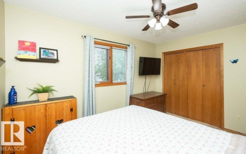 Bedroom featuring a ceiling fan with integrated lighting, wood-finish bi-fold closet doors, a window with horizontal blinds, and light-toned walls - 10711 108 Avenue, Westlock, AB - Indoor Photo Showing Bedroom