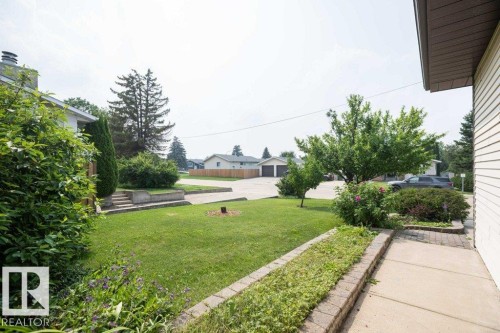 Expansive front yard featuring a manicured lawn, established trees, mature shrubs, and a paved walkway - 10711 108 Avenue, Westlock, AB - Outdoor