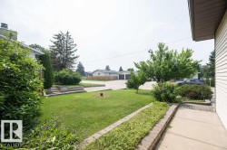 Expansive front yard featuring a manicured lawn, established trees, mature shrubs, and a paved walkway - 