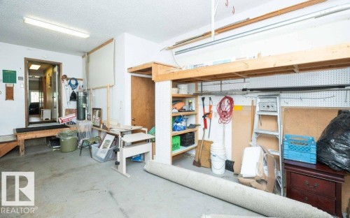 Concrete floor garage with exposed ceiling joists, overhead fluorescent lighting, built-in wooden shelving, and an interior access door - 10711 108 Avenue, Westlock, AB - Indoor