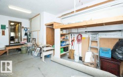 Concrete floor garage with exposed ceiling joists, overhead fluorescent lighting, built-in wooden shelving, and an interior access door - 