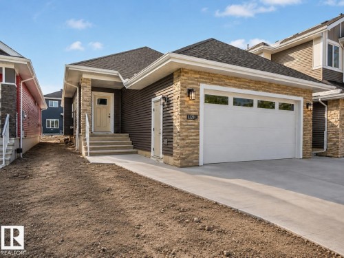 Exterior featuring a two-car garage with frosted windows, stacked stone facade accents, dark horizontal siding, concrete driveway, and a welcoming front entrance with steps and handrails - 3320 Chickadee Drive Nw, Edmonton, AB - Outdoor