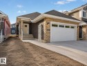 Exterior featuring a two-car garage with frosted windows, stacked stone facade accents, dark horizontal siding, concrete driveway, and a welcoming front entrance with steps and handrails - 3320 Chickadee Drive Nw, Edmonton, AB  - Outdoor 