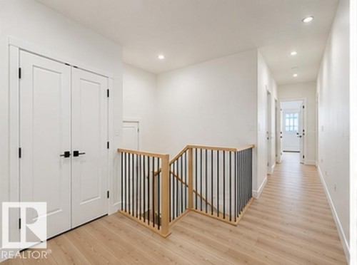 Upper-level hallway featuring light wood-finish flooring, recessed lighting, white walls, and contemporary doors with matte black hardware - 3320 Chickadee Drive Nw, Edmonton, AB - Indoor Photo Showing Other Room
